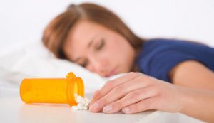 women in bed next to prescription pills